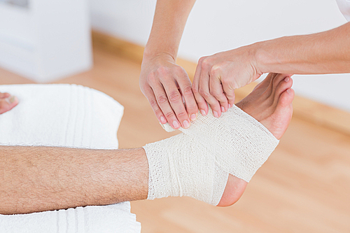 Doctor bandaging her patient ankle in medical office