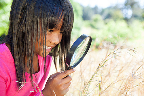 Cute little girl using magnifying glass in park on a sunny day