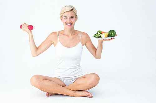 Attractive woman holding vegetables plate and dumbbell