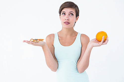 Woman choosing between pizza and an orange on white background