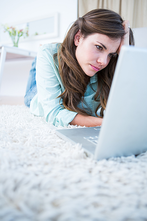 Focused woman using her laptop lying on the floor at home in the living room
