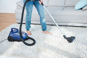 Woman using vacuum cleaner on carpet at home in the living room