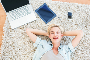 Pretty blonde woman lying on the floor and smiling at the camera in the living room