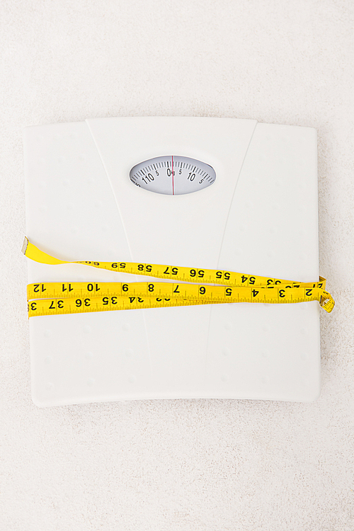 Weighing scales with measuring tape around on white background