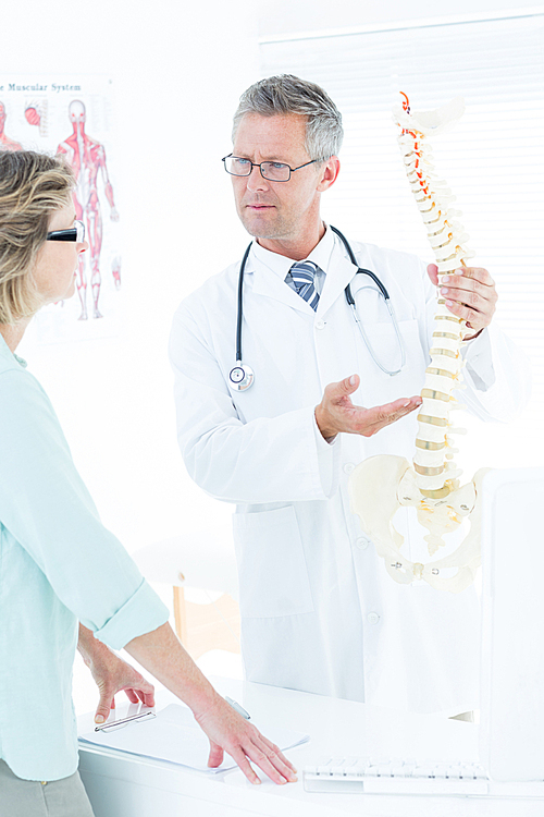 Doctor having conversation with his patient and showing spine model in medical office