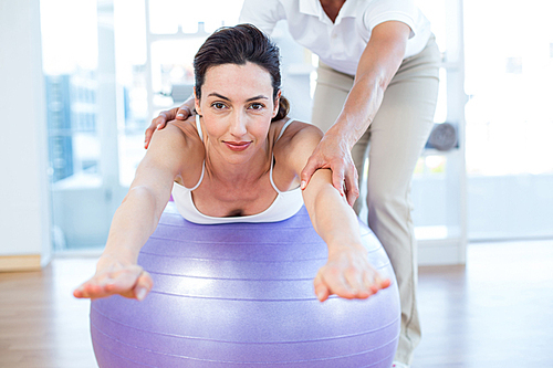 Trainer helping woman on exercise ball in medical office