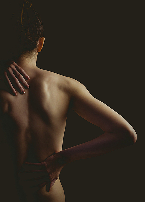 Nude woman with a back injury on black background