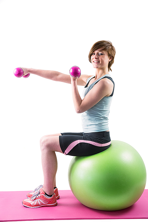 Pretty brunette  and exercising with dumbbells on fitness ball on white background