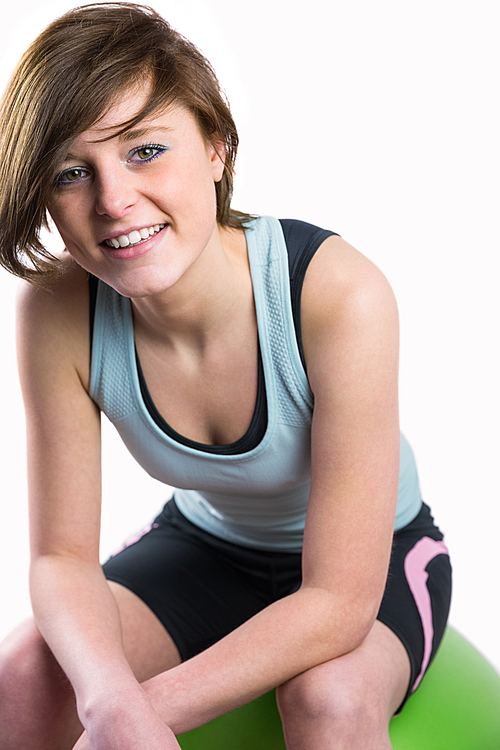 Pretty brunette  and smiling on fitness ball on white background