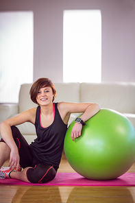 Fit woman sitting next to exercise ball at home in the living room
