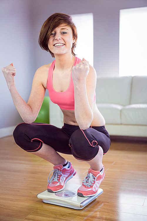 Slim woman cheering on scales in front of a sofa