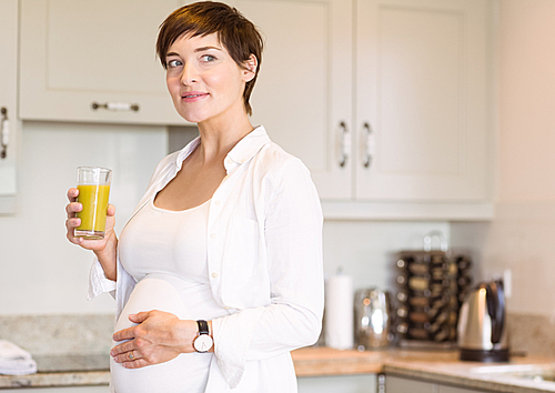 Pregnant woman having a glass of orange juice at home in the kitchen