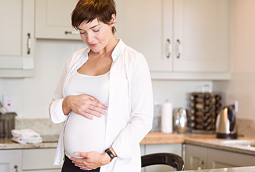 Pregnant woman holding her bump at home in the kitchen