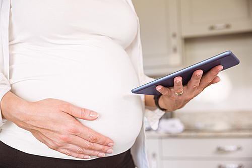 Pregnant woman using tablet pc at home in the kitchen