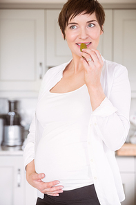 Pregnant woman eating jar of pickles at home in the kitchen