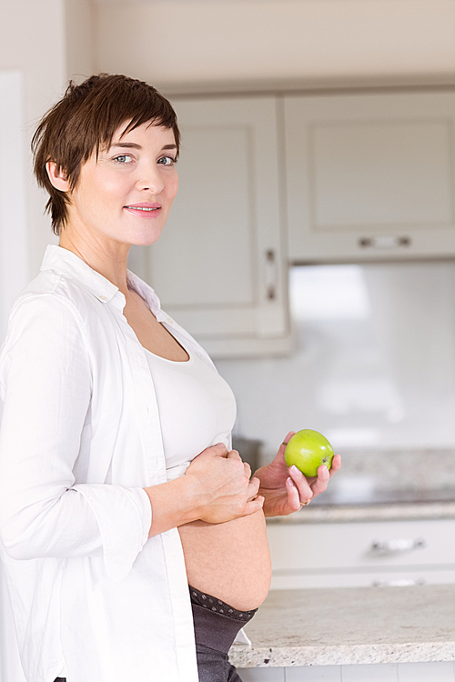 Pregnant woman holding an apple at home in the kitchen