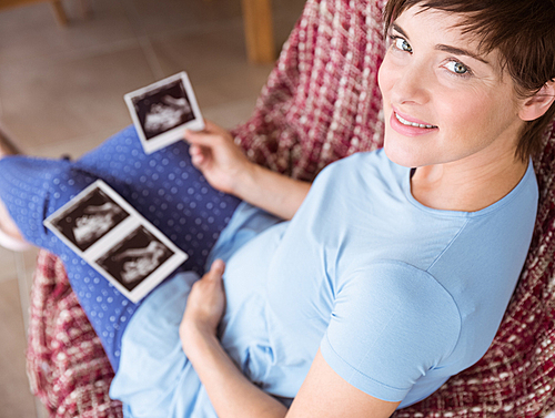 Pregnant woman looking at ultrasound scans at home in the living room