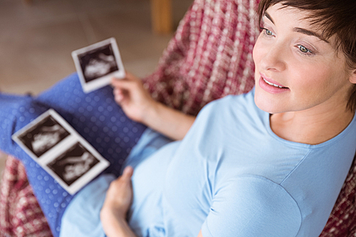 Pregnant woman looking at ultrasound scans at home in the living room