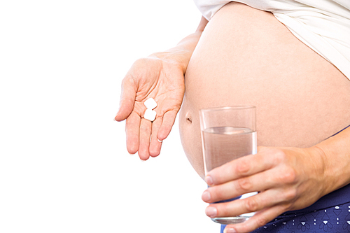 Pregnant woman taking a vitamin tablet on white background