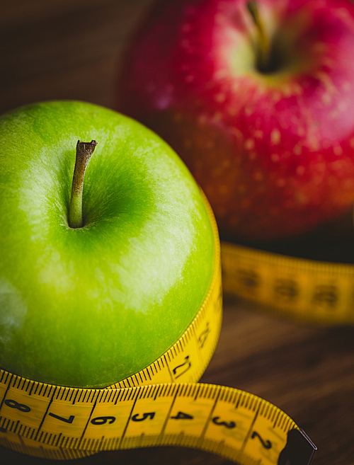 Green and red apples with measuring tape on wooden background