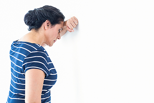 Sad woman leaning against the wall on white background