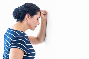 Sad woman leaning against the wall on white background