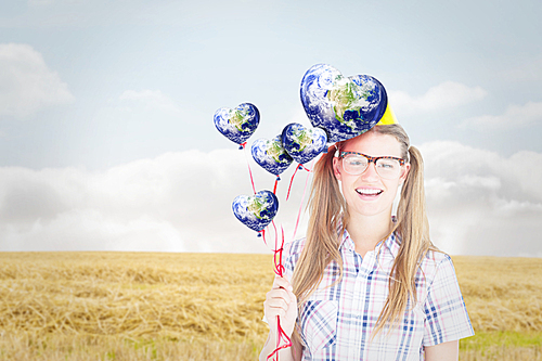 Composite image of geeky hipster smiling at camera and holding red balloons