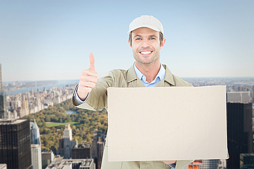 Composite image of happy delivery man gesturing thumbs up while carrying cardboard box