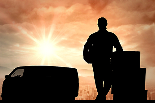 Composite image of handsome delivery man leaning on stacked cardboard boxes