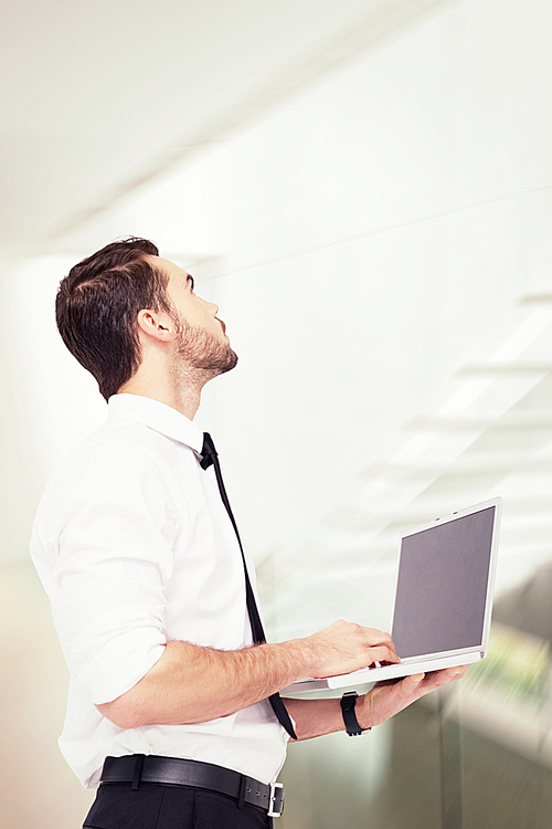 Composite image of sophisticated businessman standing using a laptop