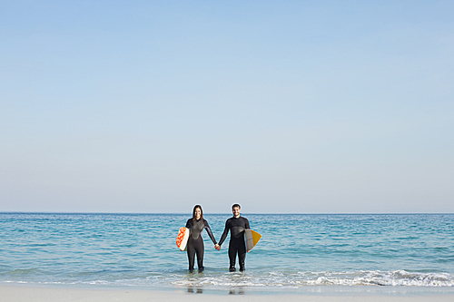 happy couple in wetsuits with surfboard on a sunny day