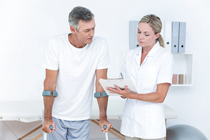 Doctor showing clipboard to her patient with crutch in medical office