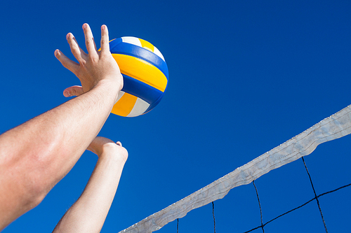 Man throwing volleyball above the net at the beach