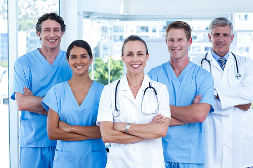 Team of doctors standing arms crossed and smiling at camera in medical office