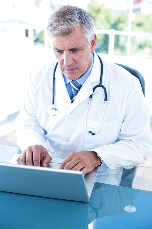 Serious doctor working on laptop at his desk in medical office