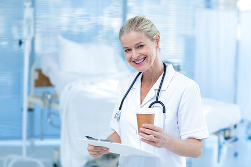 Beautiful smiling doctor holding clipboard and goblet in hospital room