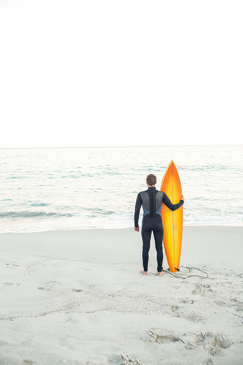 Man in wetsuit with a surfboard on a sunny day at the beach