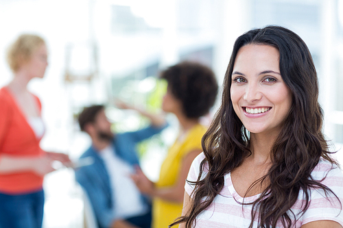 Portrait of smiling young businesswoman with colleagues in background at the office