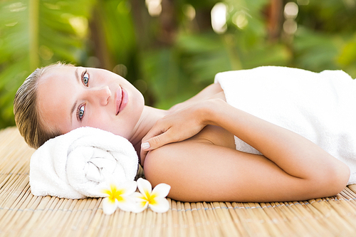 Peaceful blonde lying on bamboo mat with flowers at the health spa