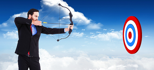 Focused businessman shooting a bow and arrow against bright blue sky with clouds