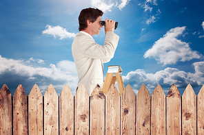 Businessman looking on a ladder against fence under blue sky