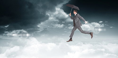 Businessman jumping holding an umbrella against bright blue sky with clouds