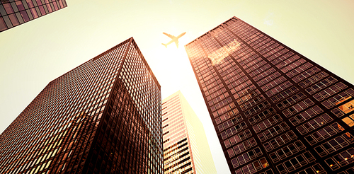 An airplane flying over buildings with the sun shining