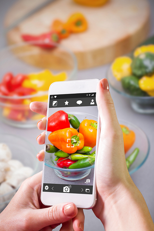 Hand holding smartphone against close up of pimentos