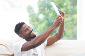 Man using his tablet on couch to take selfie at home in the living room