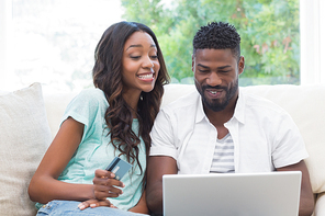 Happy couple on the couch shopping online at home in the living room