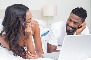 Relaxed couple using laptop on bed at home in bedroom