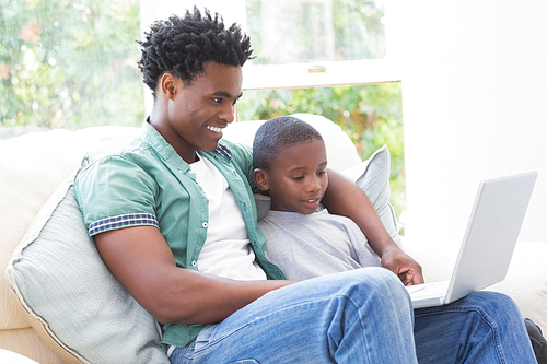 Father and son using laptop on the couch at home in the living room