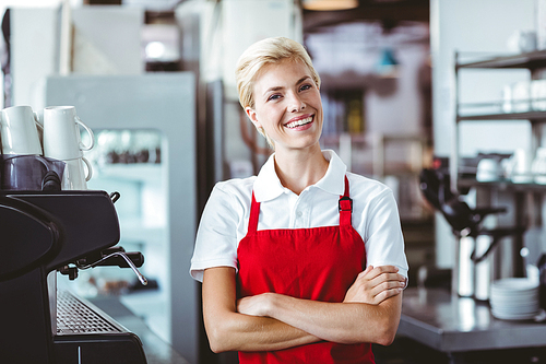 Pretty barista smiling at the camera with arms crossed