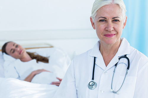 Female doctor smiling at camera while her patient sleeping in hospital